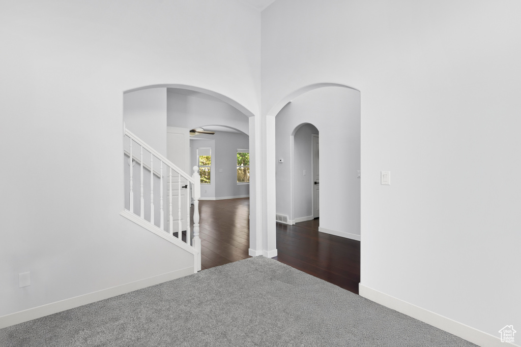 Empty room featuring carpet floors, a ceiling fan, arched walkways, baseboards, and stairs