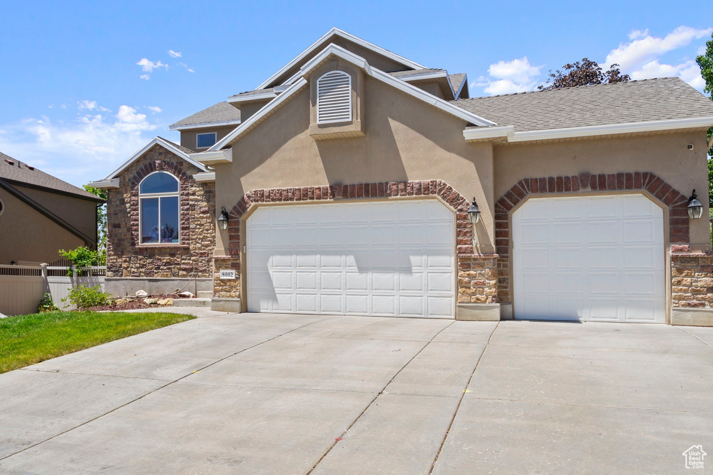 View of front of property featuring stone siding, an attached garage, driveway, stucco siding, and a shingled roof