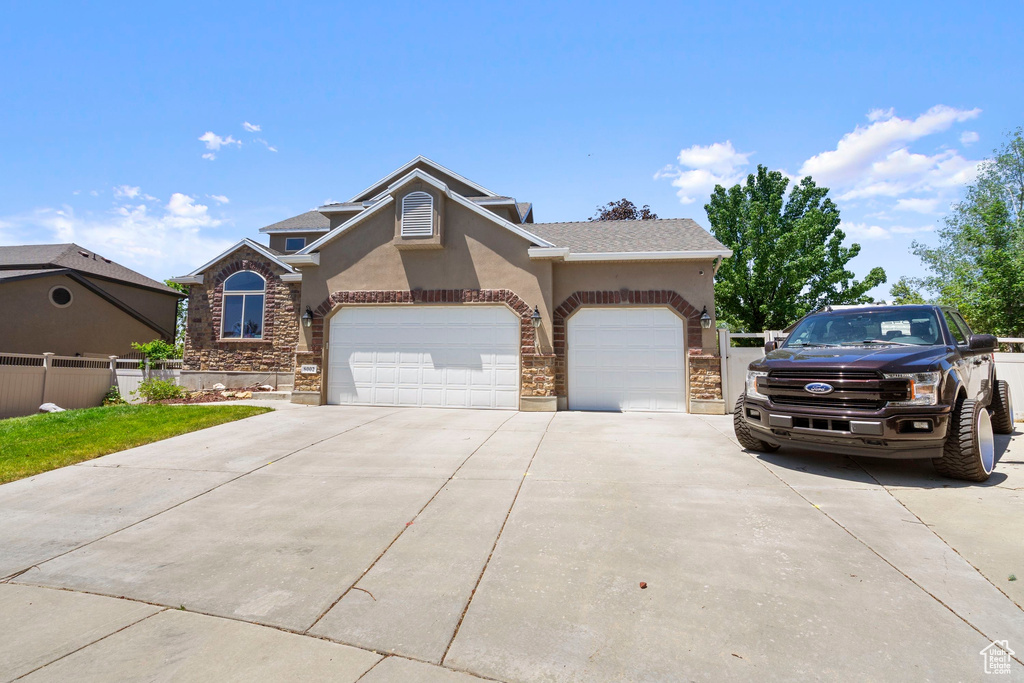 View of front of house featuring stucco siding, driveway, an attached garage, and stone siding