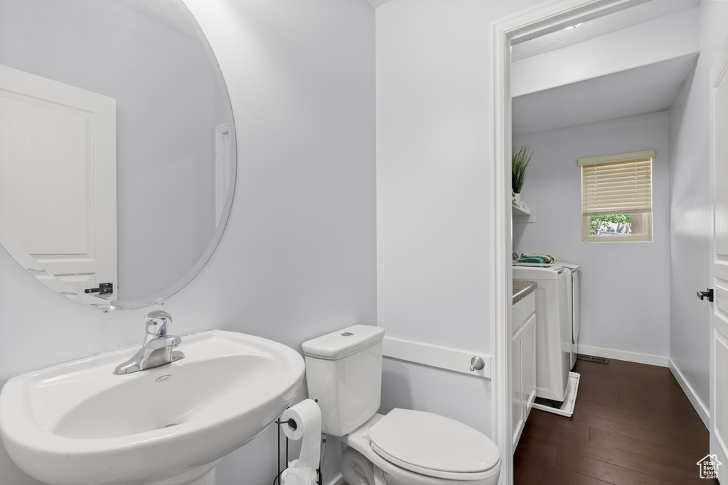 Bathroom featuring washing machine and clothes dryer, a sink, toilet, and wood finished floors