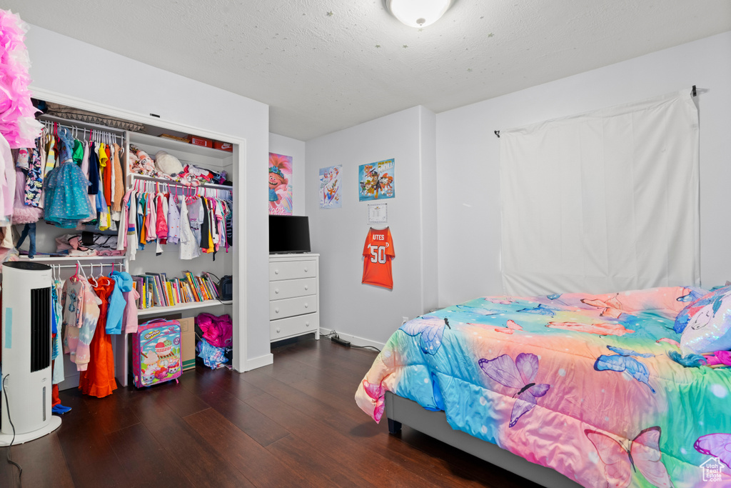 Bedroom with wood finished floors, baseboards, a closet, water heater, and a textured ceiling