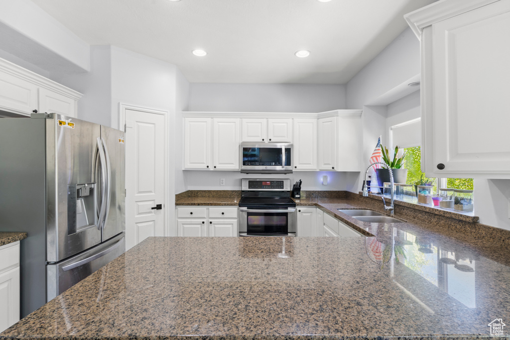 Kitchen featuring appliances with stainless steel finishes, a sink, white cabinets, dark stone countertops, and a peninsula