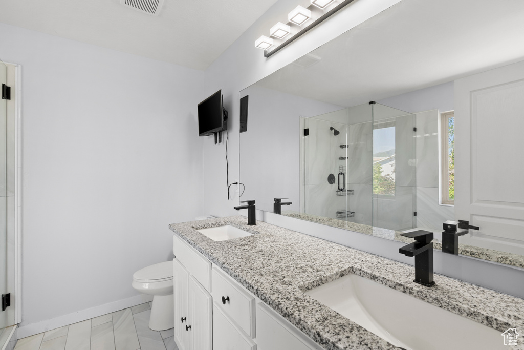 Full bath featuring a stall shower, toilet, double vanity, and baseboards