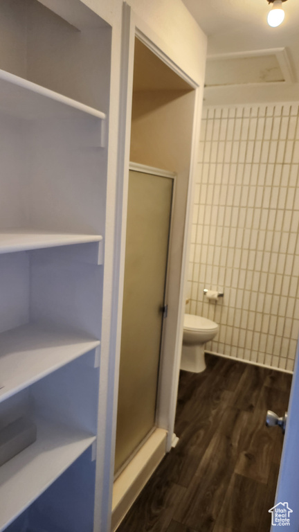 Bathroom featuring toilet, a stall shower, and wood finished floors
