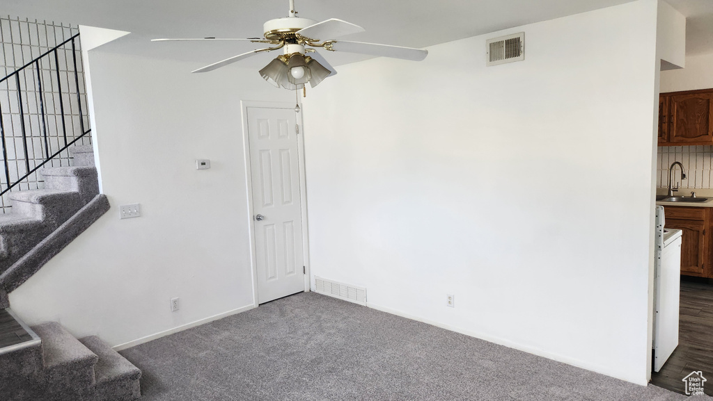 Unfurnished room featuring a ceiling fan, a sink, stairway, and dark carpet