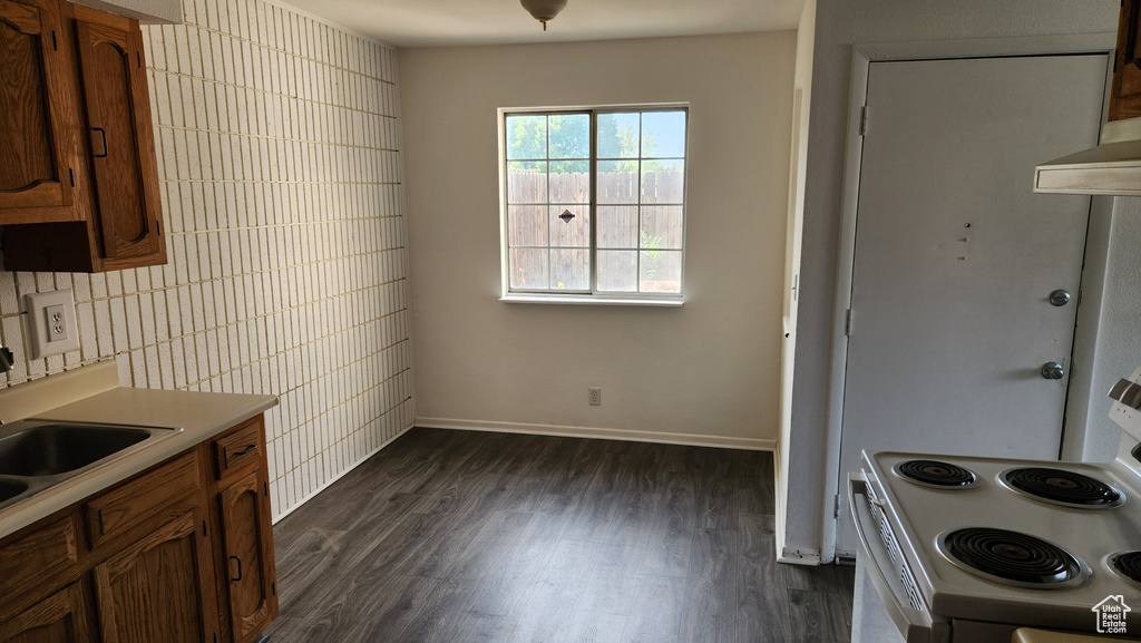 Kitchen with white range with electric stovetop, dark wood-type flooring, light countertops, brown cabinetry, and tile walls
