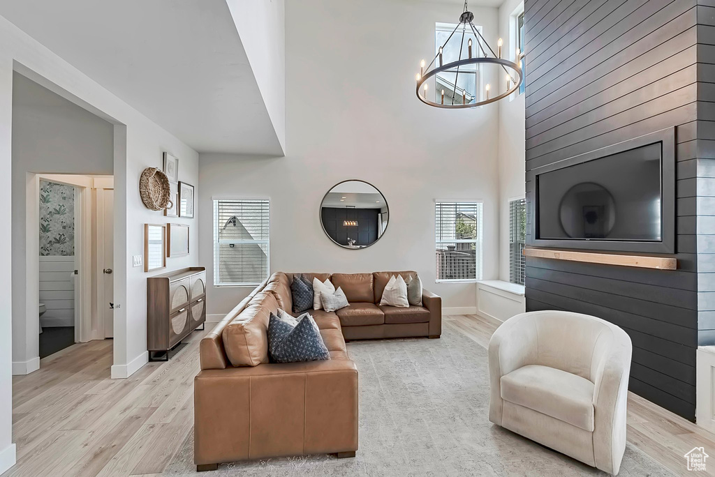 Living area with light wood-type flooring, a chandelier, baseboards, and a towering ceiling