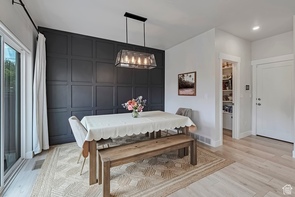 Dining area featuring a decorative wall, light wood finished floors, a chandelier, and baseboards