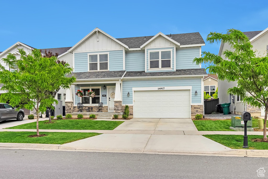 Craftsman-style home featuring driveway, stone siding, a front yard, board and batten siding, and covered porch