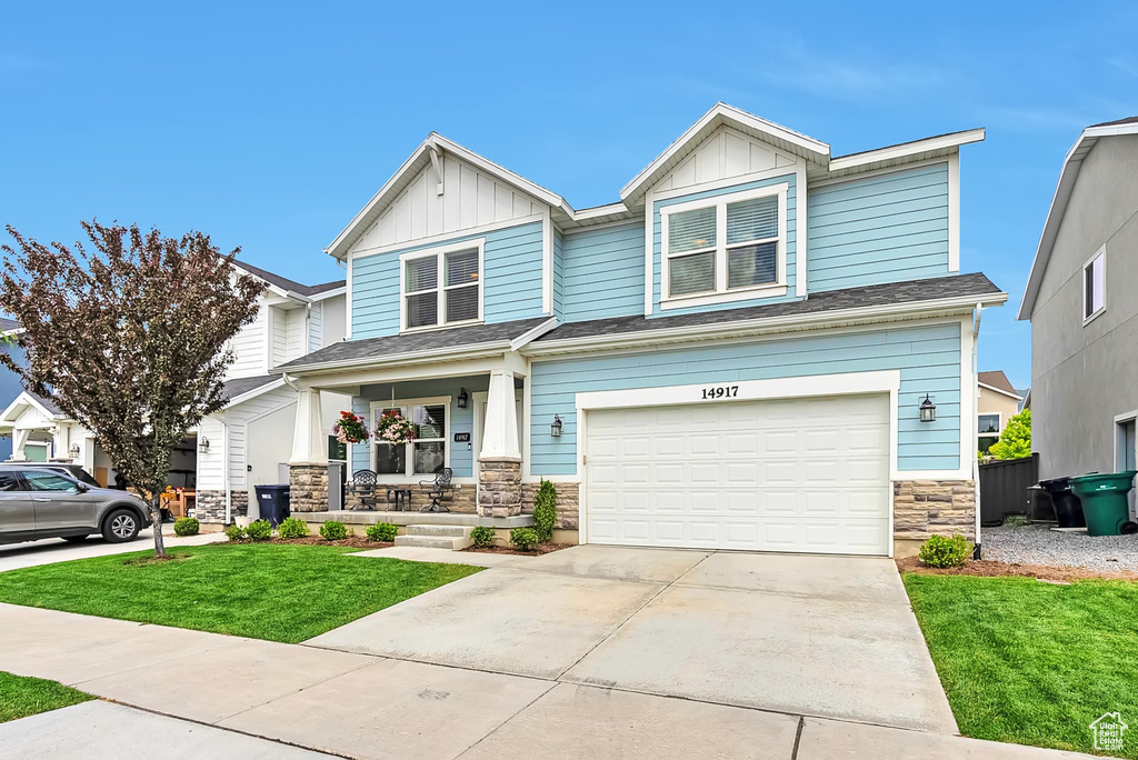 Craftsman house featuring stone siding, covered porch, a front lawn, and board and batten siding