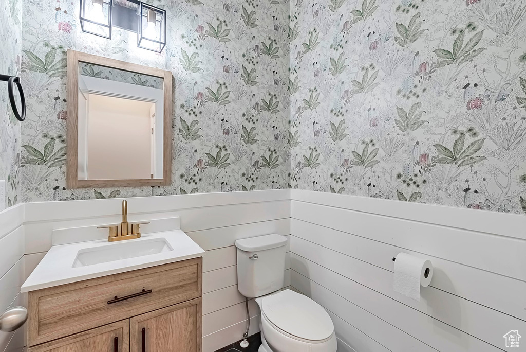 Half bathroom with wallpapered walls, a wainscoted wall, toilet, and vanity
