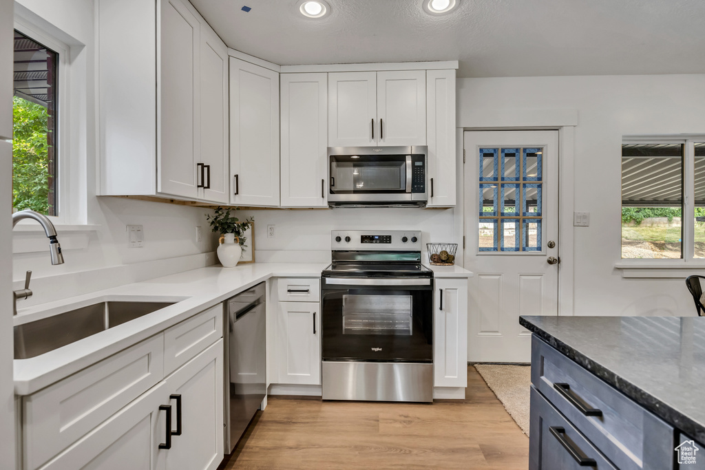 Kitchen with stainless steel appliances, a sink, recessed lighting, white cabinetry, and light wood-type flooring