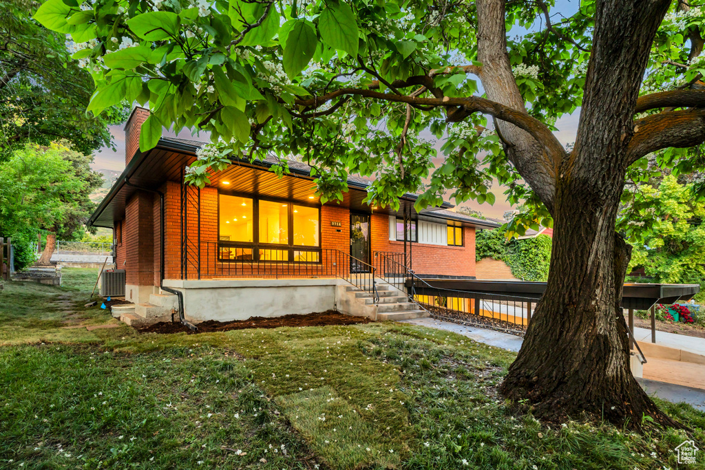 View of front facade featuring brick siding, a front lawn, a chimney, and central air condition unit