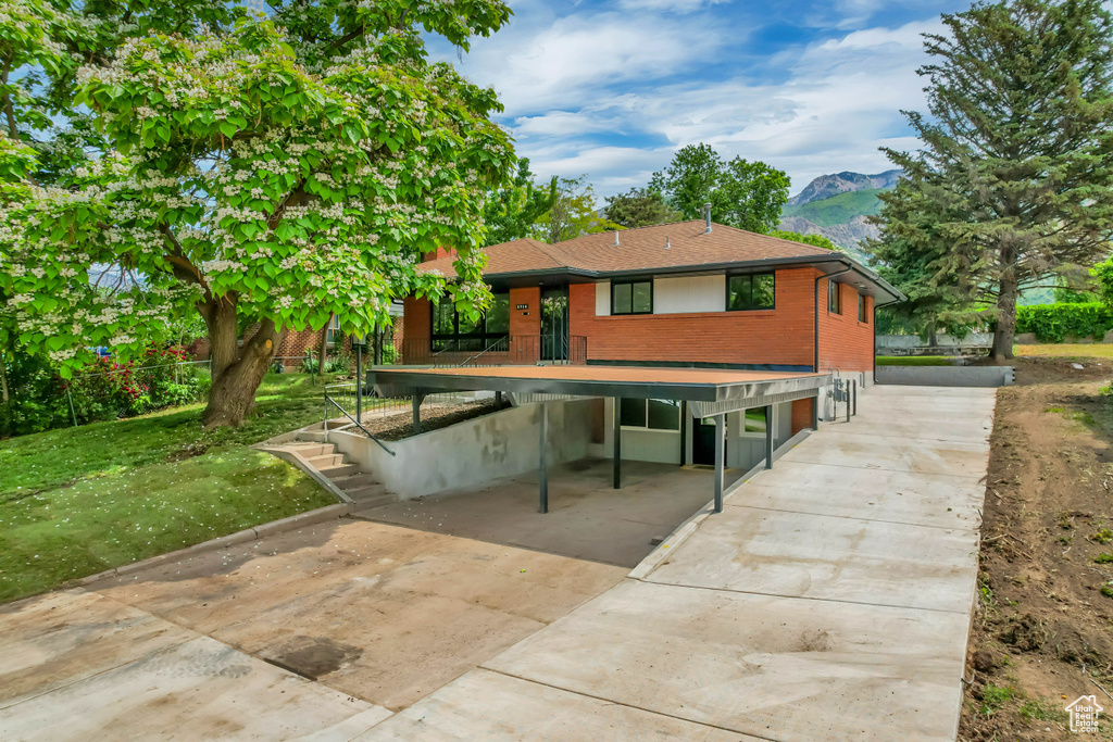 Rear view of house with driveway, a mountain view, a carport, brick siding, and a shingled roof