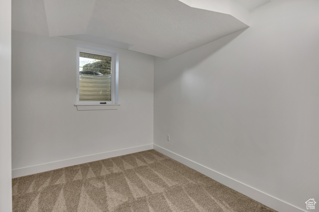 Empty room featuring carpet floors, baseboards, and vaulted ceiling