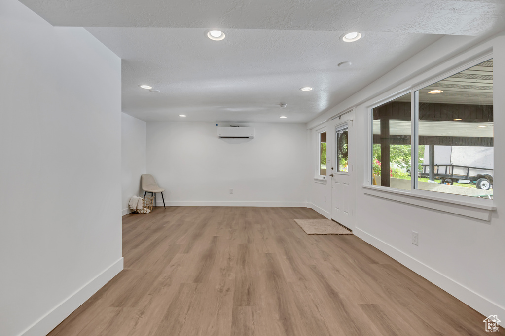 Empty room with a wall mounted AC, recessed lighting, light wood-type flooring, and baseboards
