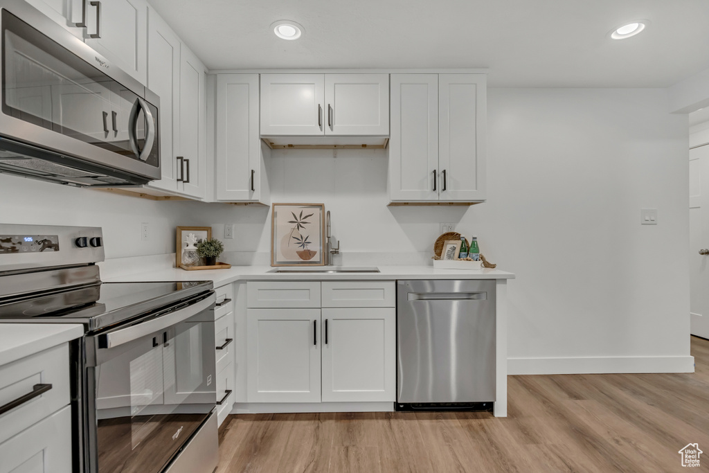 Kitchen featuring stainless steel appliances, a sink, light countertops, light wood-type flooring, and baseboards