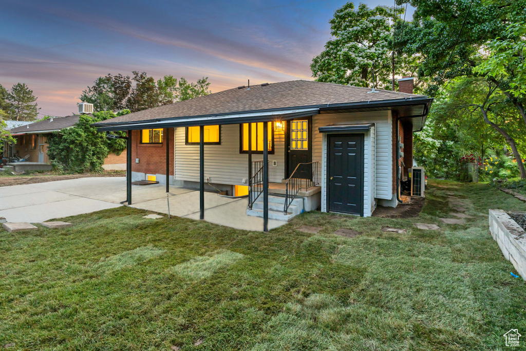Back of house with a chimney, a lawn, a patio area, and a shingled roof