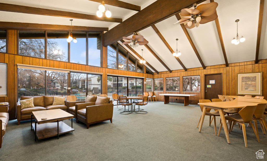 Carpeted living room with beamed ceiling, wooden walls, a ceiling fan, high vaulted ceiling, and a chandelier