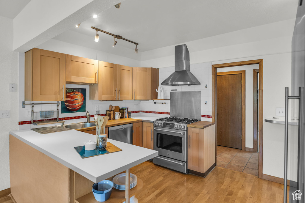 Kitchen featuring wall chimney range hood, appliances with stainless steel finishes, a peninsula, and backsplash