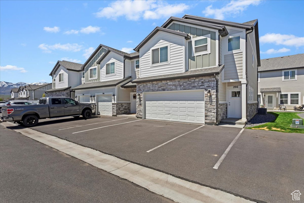 Townhome / multi-family property with board and batten siding, stone siding, a residential view, a garage, and asphalt driveway