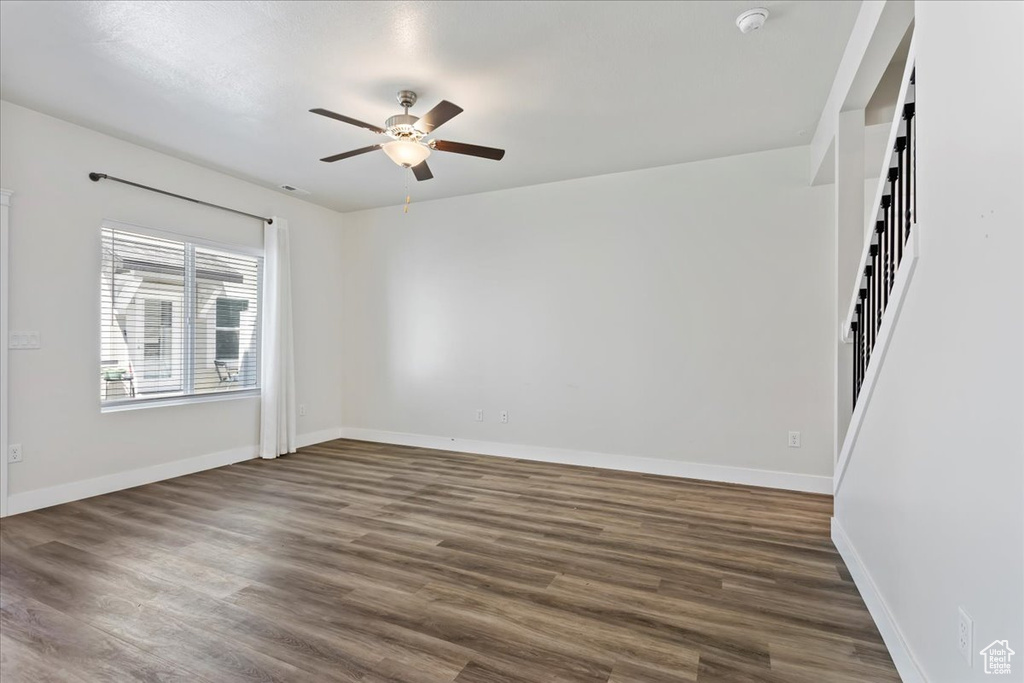 Unfurnished room featuring a ceiling fan, dark wood-style floors, baseboards, a smoke detector, and stairway