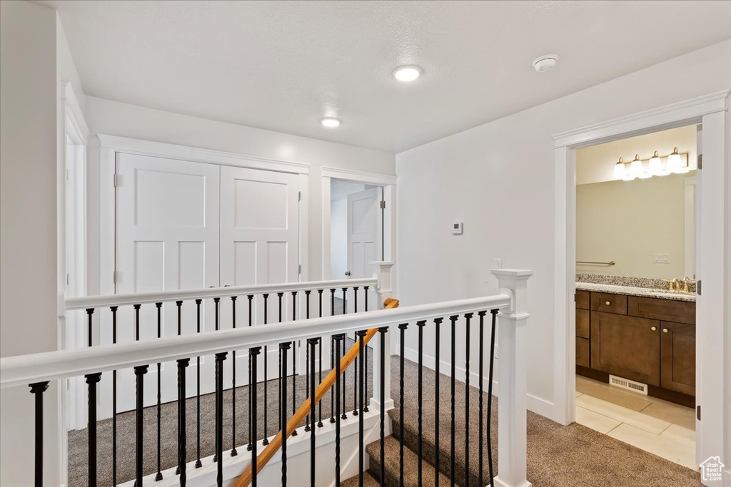 Hall featuring an upstairs landing, light colored carpet, a sink, light tile patterned flooring, and recessed lighting