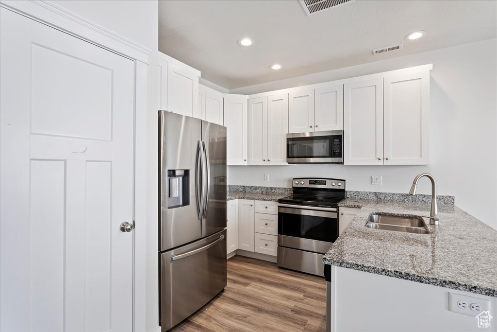 Kitchen with stainless steel appliances, a sink, recessed lighting, light stone countertops, and white cabinetry