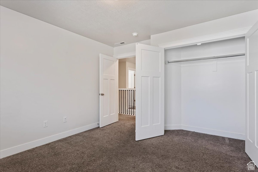 Unfurnished bedroom featuring dark colored carpet, baseboards, and a closet