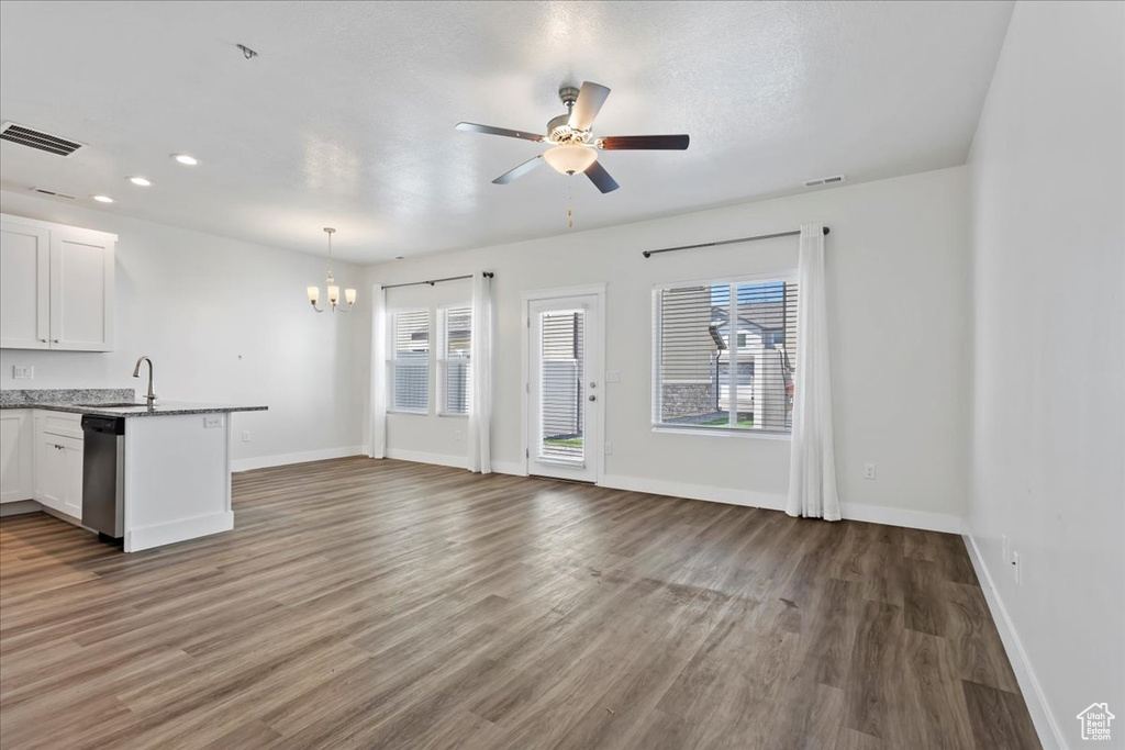 Unfurnished living room with a chandelier, plenty of natural light, wood finished floors, baseboards, and recessed lighting
