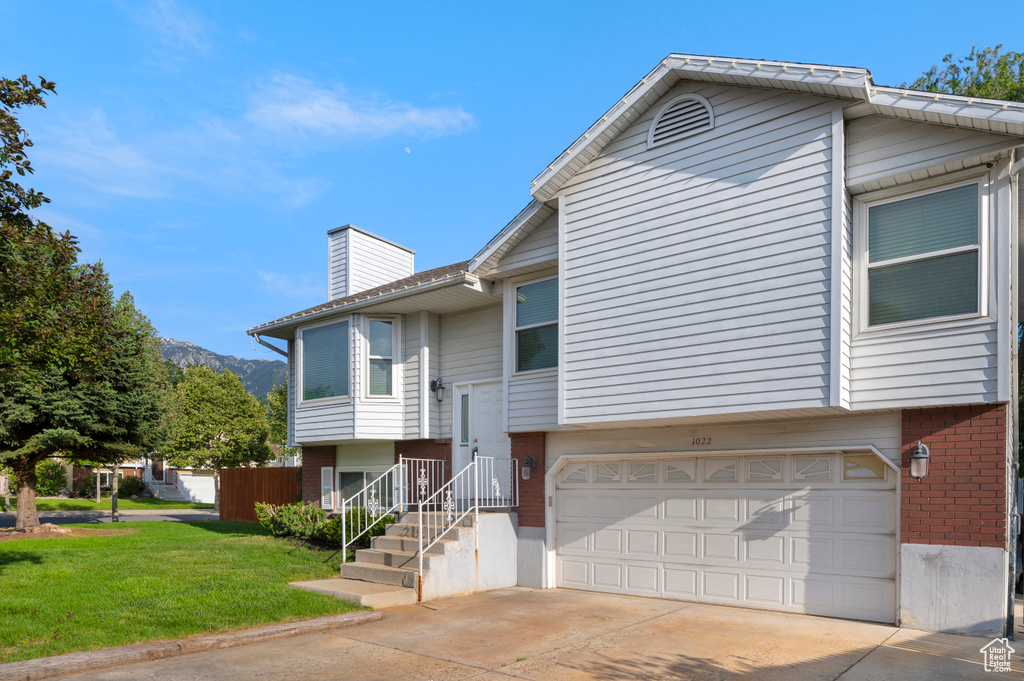 Split foyer home with brick siding, a garage, a chimney, a front lawn, and concrete driveway