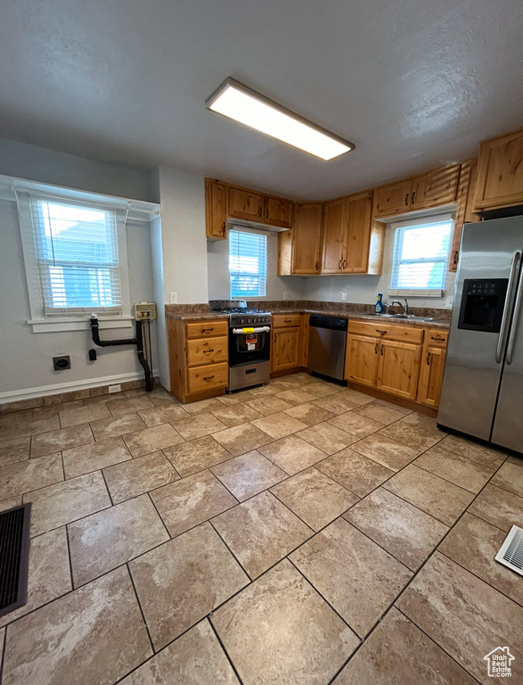 Kitchen with stainless steel appliances, dark countertops, baseboards, a sink, and brown cabinetry
