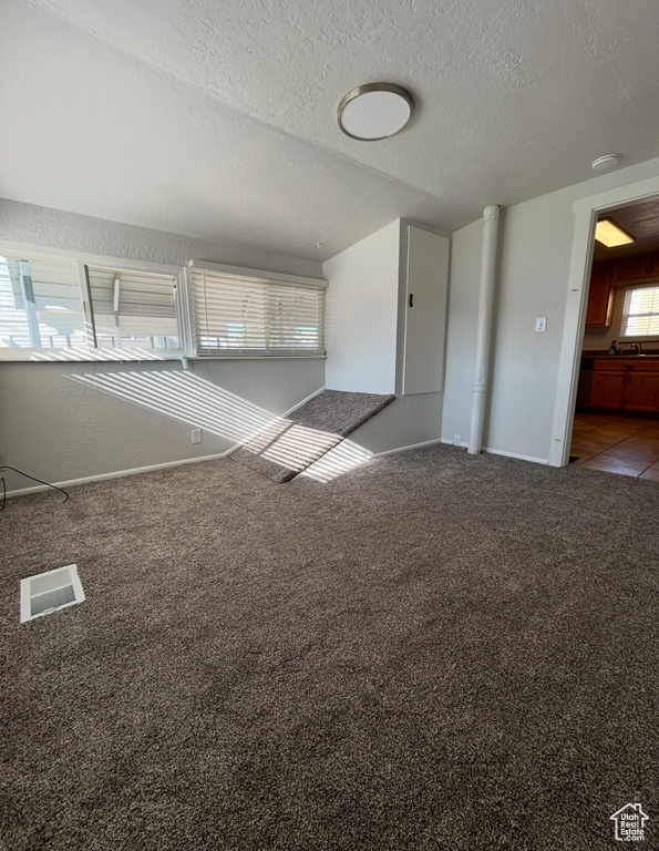 Carpeted spare room featuring a textured ceiling and baseboards