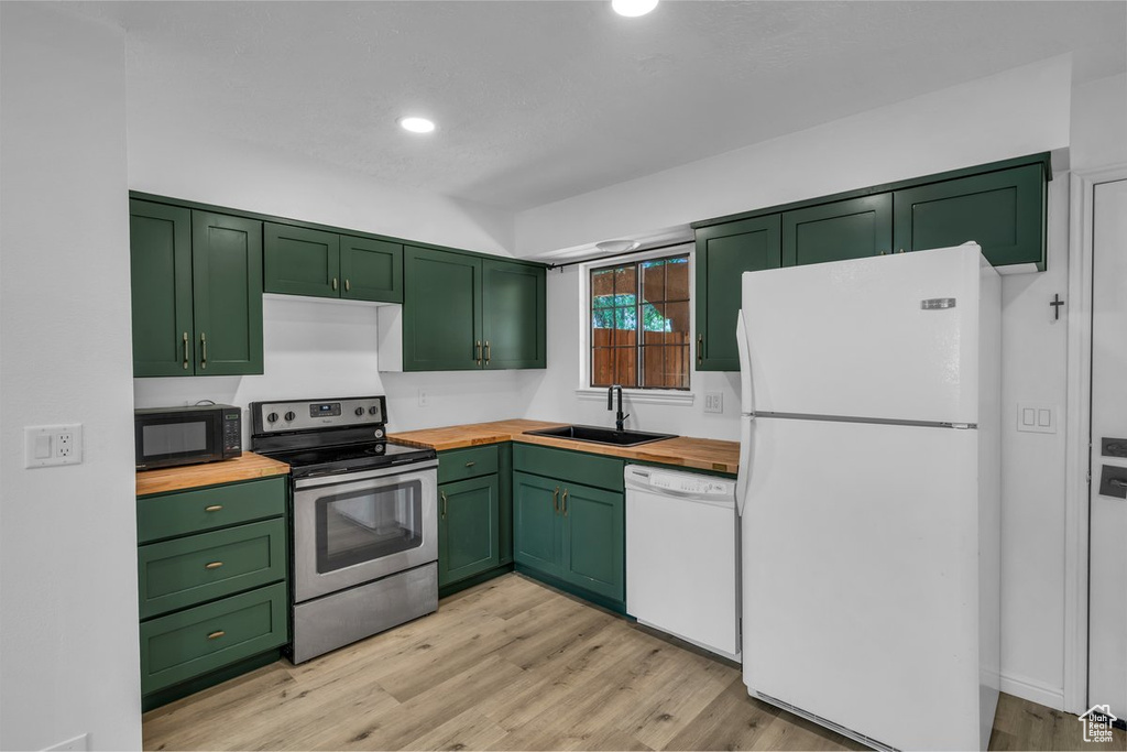 Kitchen featuring white appliances, green cabinets, butcher block counters, a sink, and light wood-style flooring