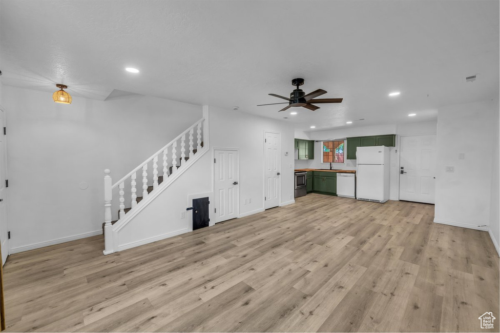 Unfurnished living room featuring stairway, a ceiling fan, light wood-type flooring, recessed lighting, and baseboards