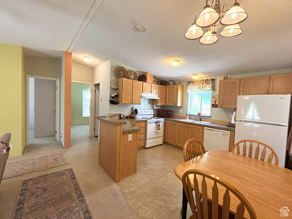 Kitchen featuring white appliances, a sink, a chandelier, under cabinet range hood, and dark countertops
