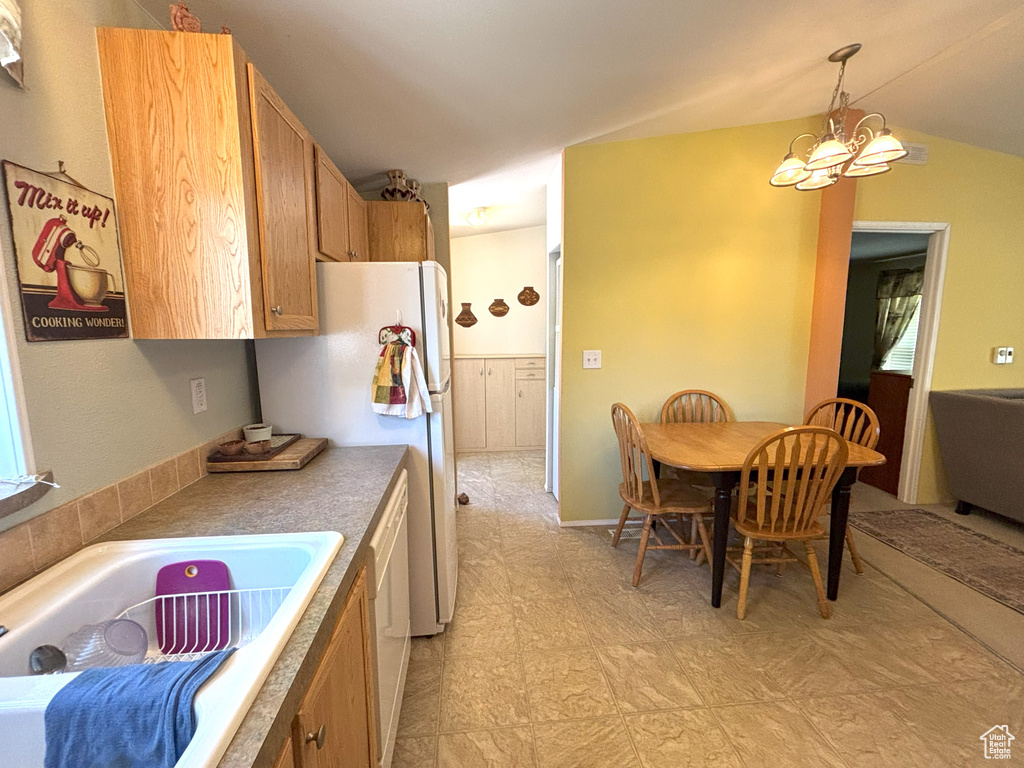 Kitchen with a chandelier, decorative light fixtures, freestanding refrigerator, vaulted ceiling, and a sink