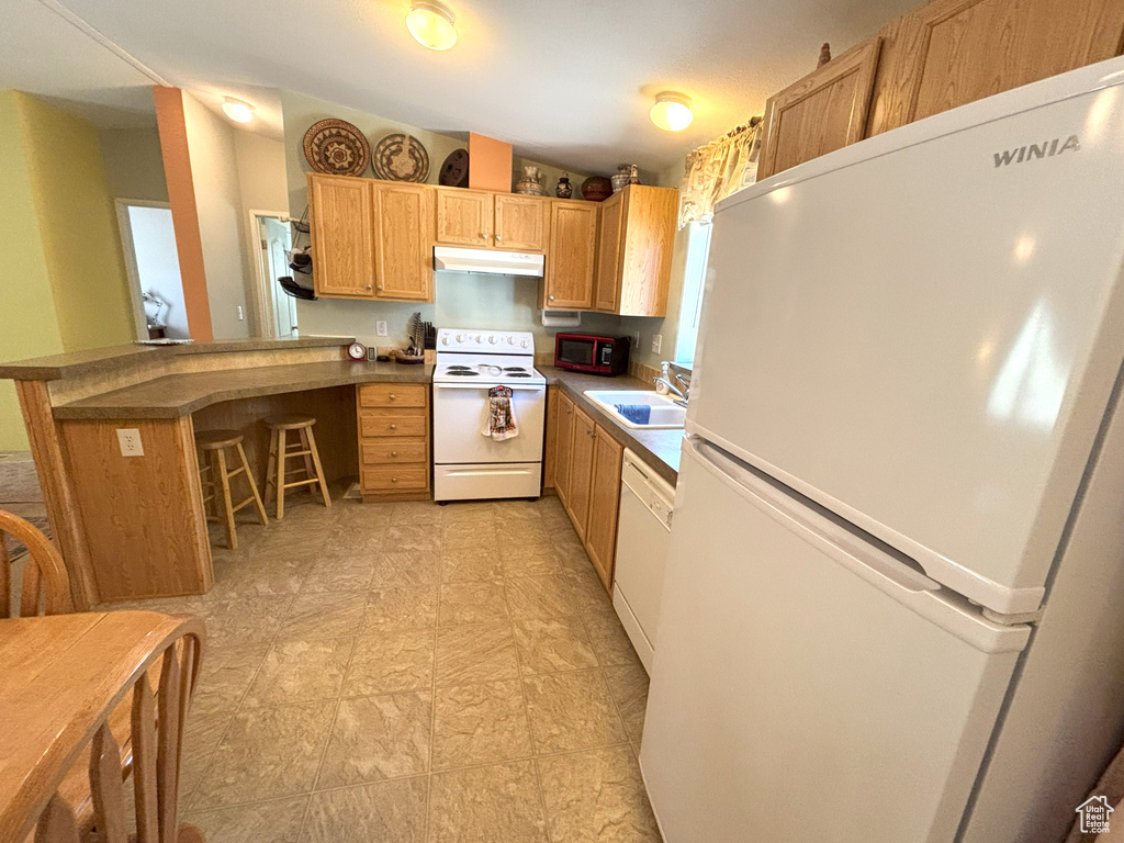 Kitchen featuring white appliances, under cabinet range hood, a sink, a peninsula, and a breakfast bar area