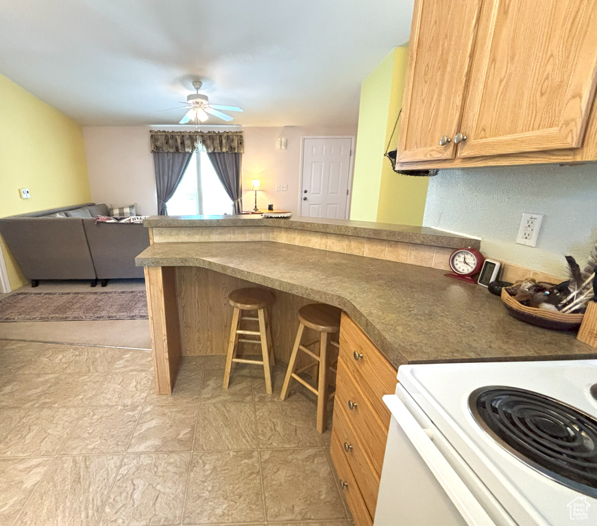 Kitchen featuring range with electric cooktop, a peninsula, open floor plan, ceiling fan, and a kitchen breakfast bar