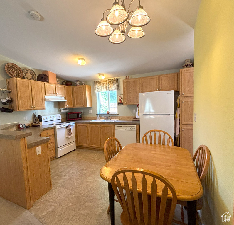 Kitchen featuring white appliances, a chandelier, under cabinet range hood, a sink, and dark countertops