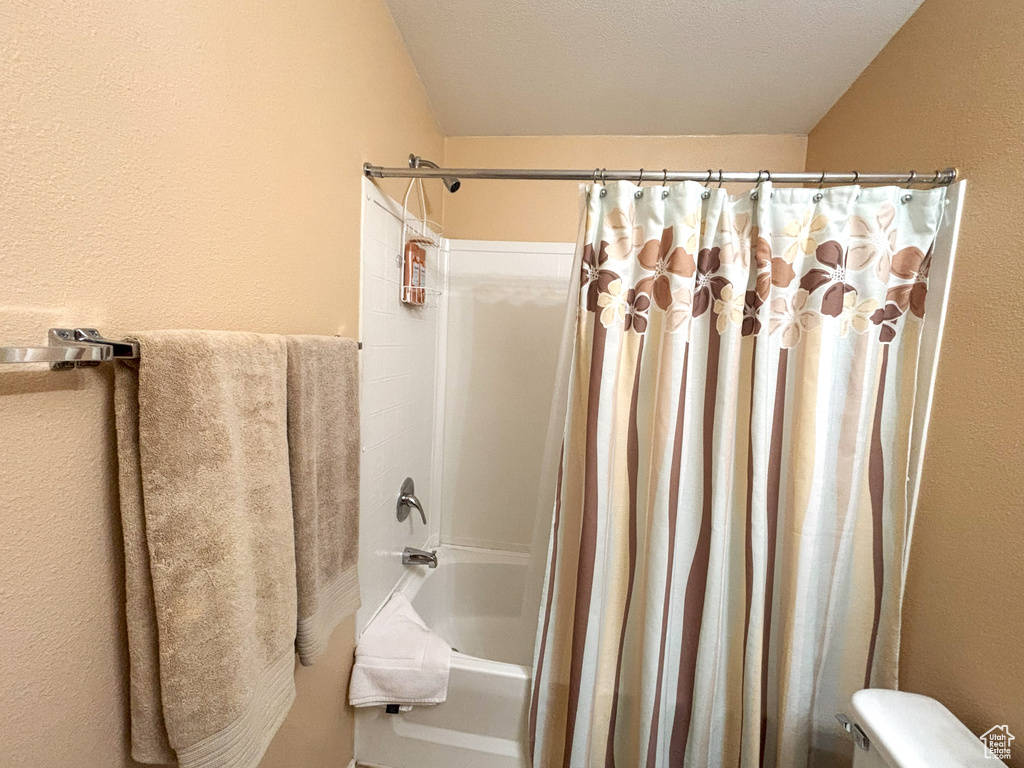 Full bath with shower / bath combo, toilet, and a textured wall