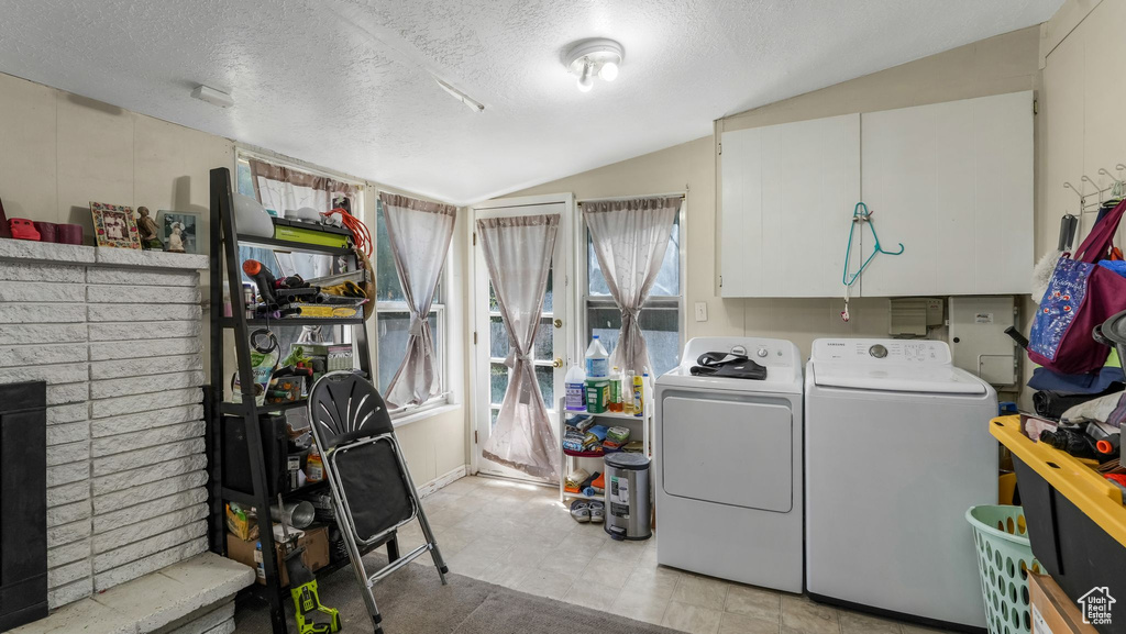 Laundry area featuring washing machine and clothes dryer, a textured ceiling, light floors, and a fireplace