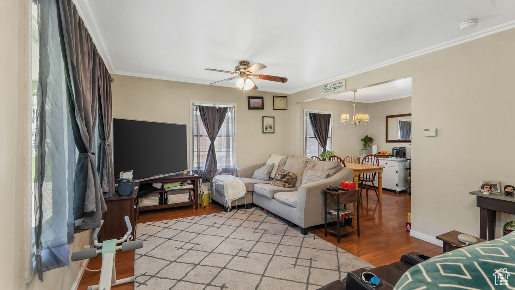 Living area featuring light wood-type flooring, a ceiling fan, a chandelier, crown molding, and baseboards