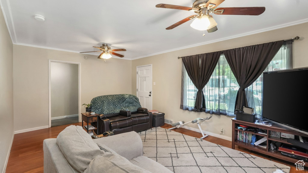 Living room featuring a ceiling fan, crown molding, baseboards, and wood finished floors