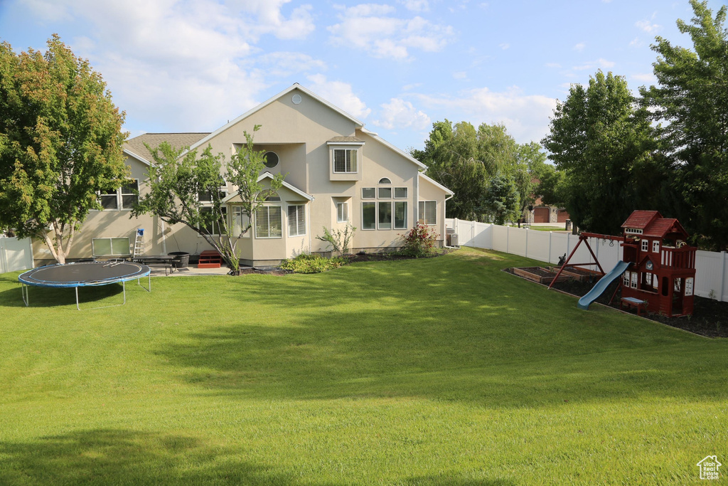 Back of property with a trampoline, a playground, and stucco siding