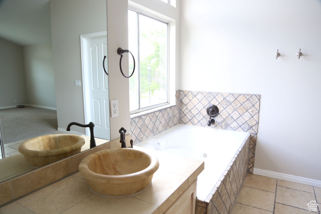 Full bathroom with healthy amount of natural light, a jetted tub, a sink, and baseboards