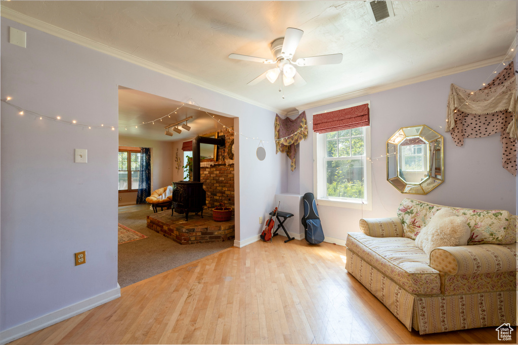 Living area with a wood stove, plenty of natural light, wood finished floors, ceiling fan, and crown molding
