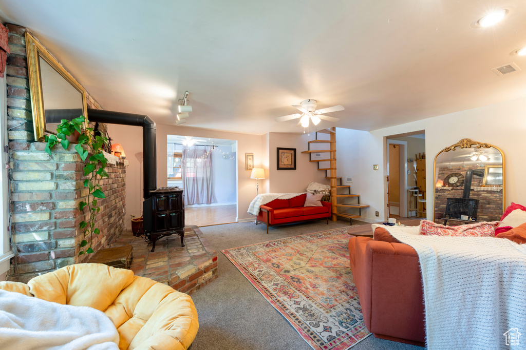 Carpeted living room with a wood stove, ceiling fan, and baseboards