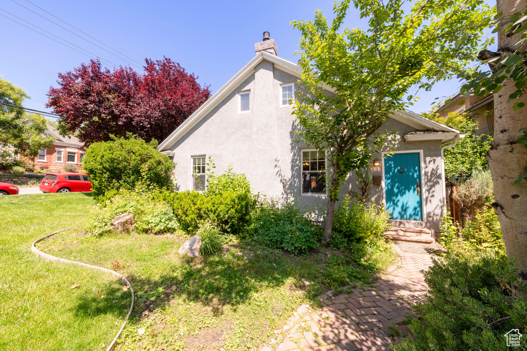 View of front of home with stucco siding, a chimney, and a front lawn