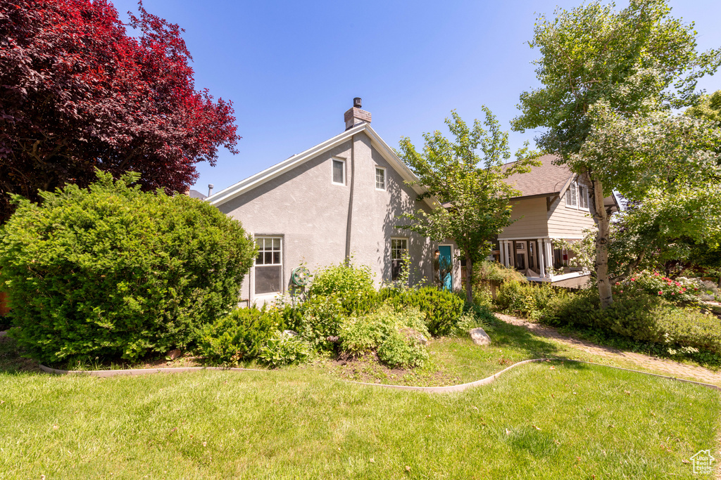 Back of house featuring a chimney, stucco siding, and a lawn